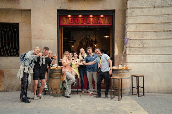 Group enjoying local delicacies and drinks in a historic bar during a Barcelona food tour.