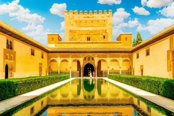 Alhambra's Nasrid Palaces with intricate Moorish arches and a reflective pool in the Court of the Myrtles, Granada, Spain.