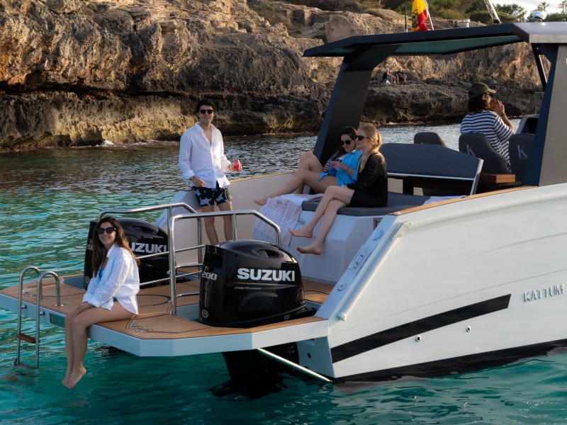 Group of friends relaxing at the stern of the catamaran anchored in a cove
